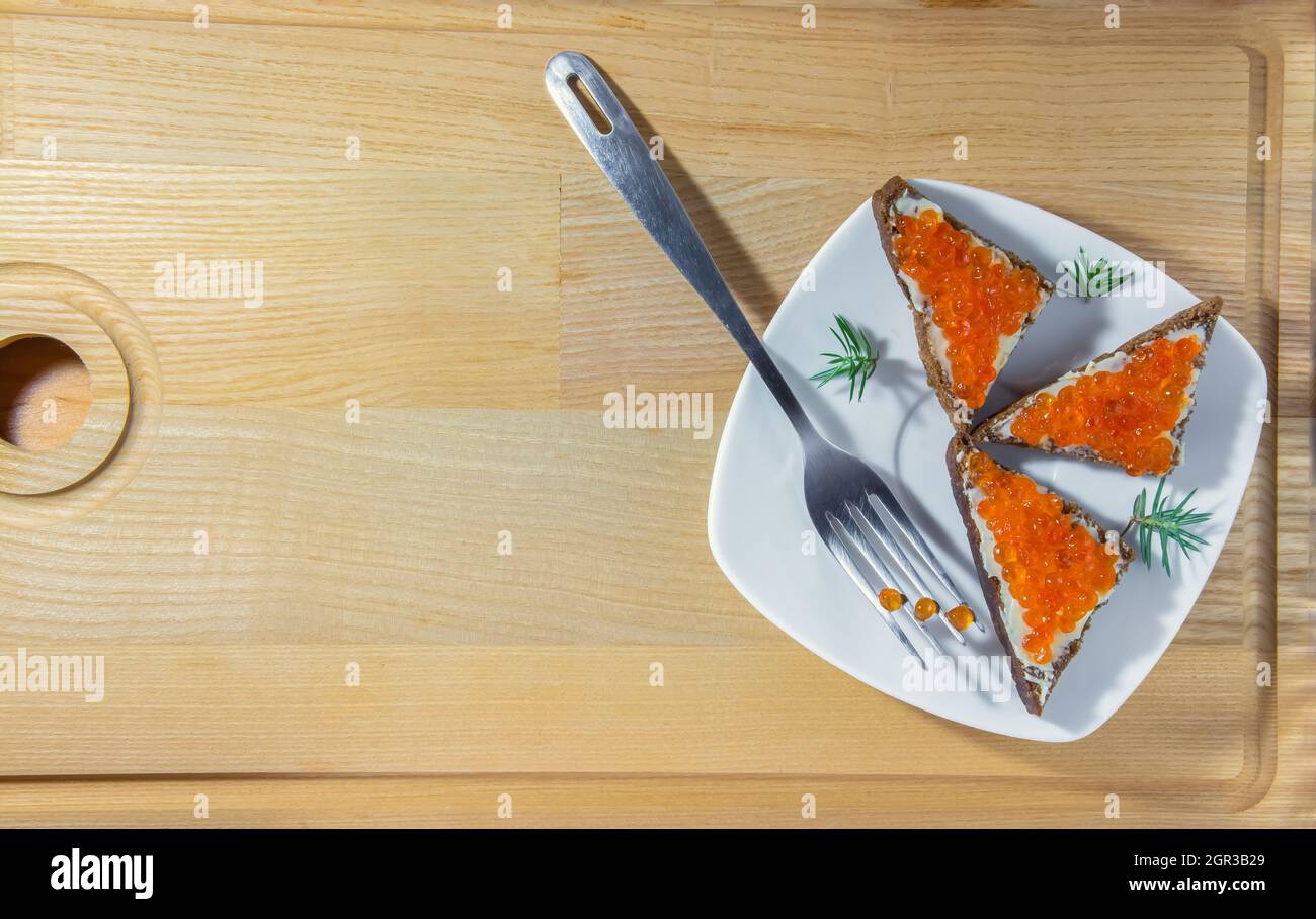Small sandwiches with caviar in the shape of a triangle on a white square plate with a fork on a wooden background. High quality photo Stock Photo