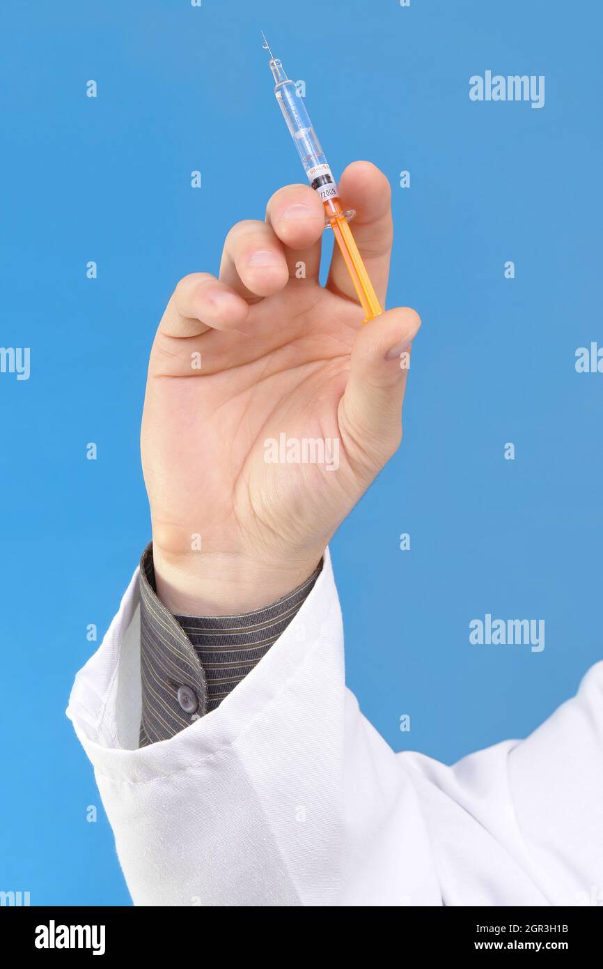Doctor's Hand Holding Syringe With Needle Over Blue Background Stock Photo