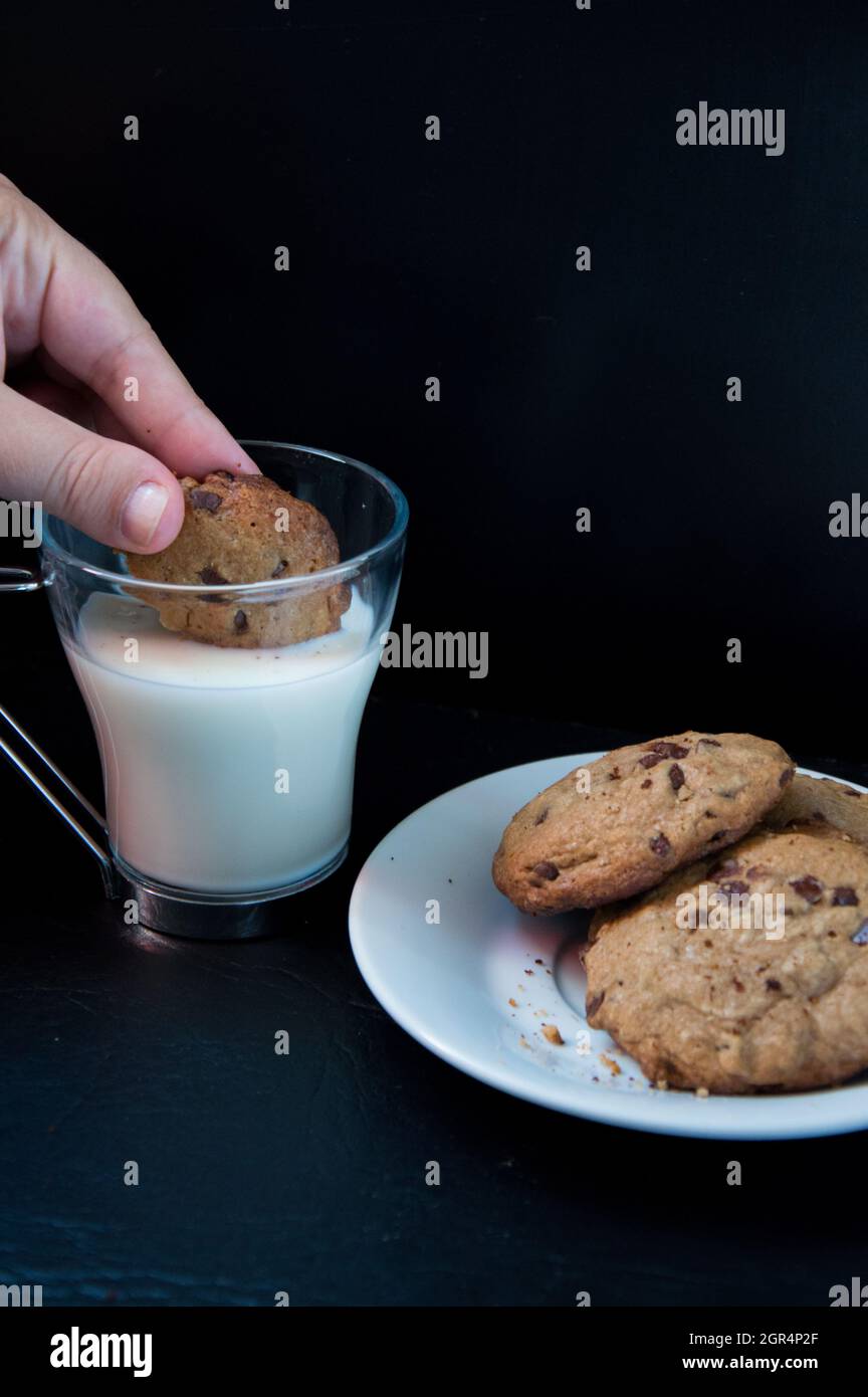 Close-up Of Hand Holding Chocolate Cookie On Glass Of Milk Stock Photo