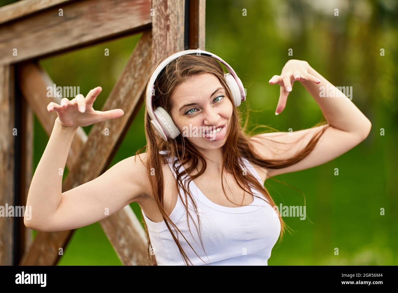 Woman 29 years old in wireless headphones is grimacing in park. Stock Photo