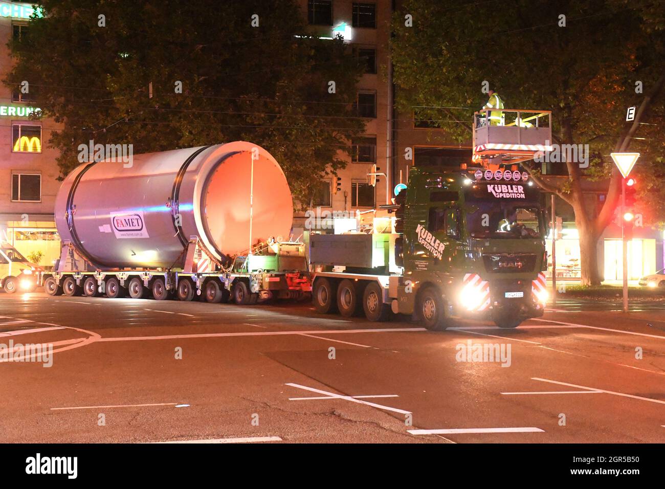 Munich, Germany. 30th Sep, 2021. A heavy goods vehicle is transporting a large silo to the Munich South CHP plant. On the way, the team turns off in Sonnenstraße towards Schwanthalerstraße, while the tramway's overhead lines are being lifted with a lifting platform. The transport started during the night via the route Ingolstädter Straße towards Leopoldstraße through the city centre, via Sonnenstraße towards Theresienhöhe, Brudermühlstraße to the combined heat and power plant in Schäftlarnstraße. Credit: Felix Hörhager/dpa/Alamy Live News Stock Photo