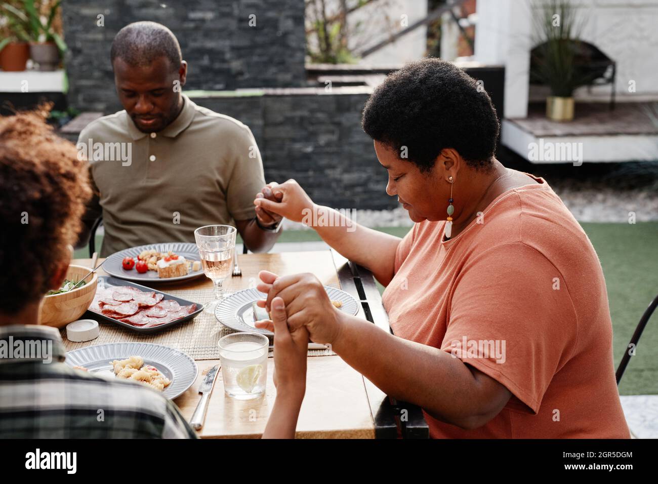 Portrait of senior African-American woman holding hands with family at dinner outdoors and praying, copy space Stock Photo