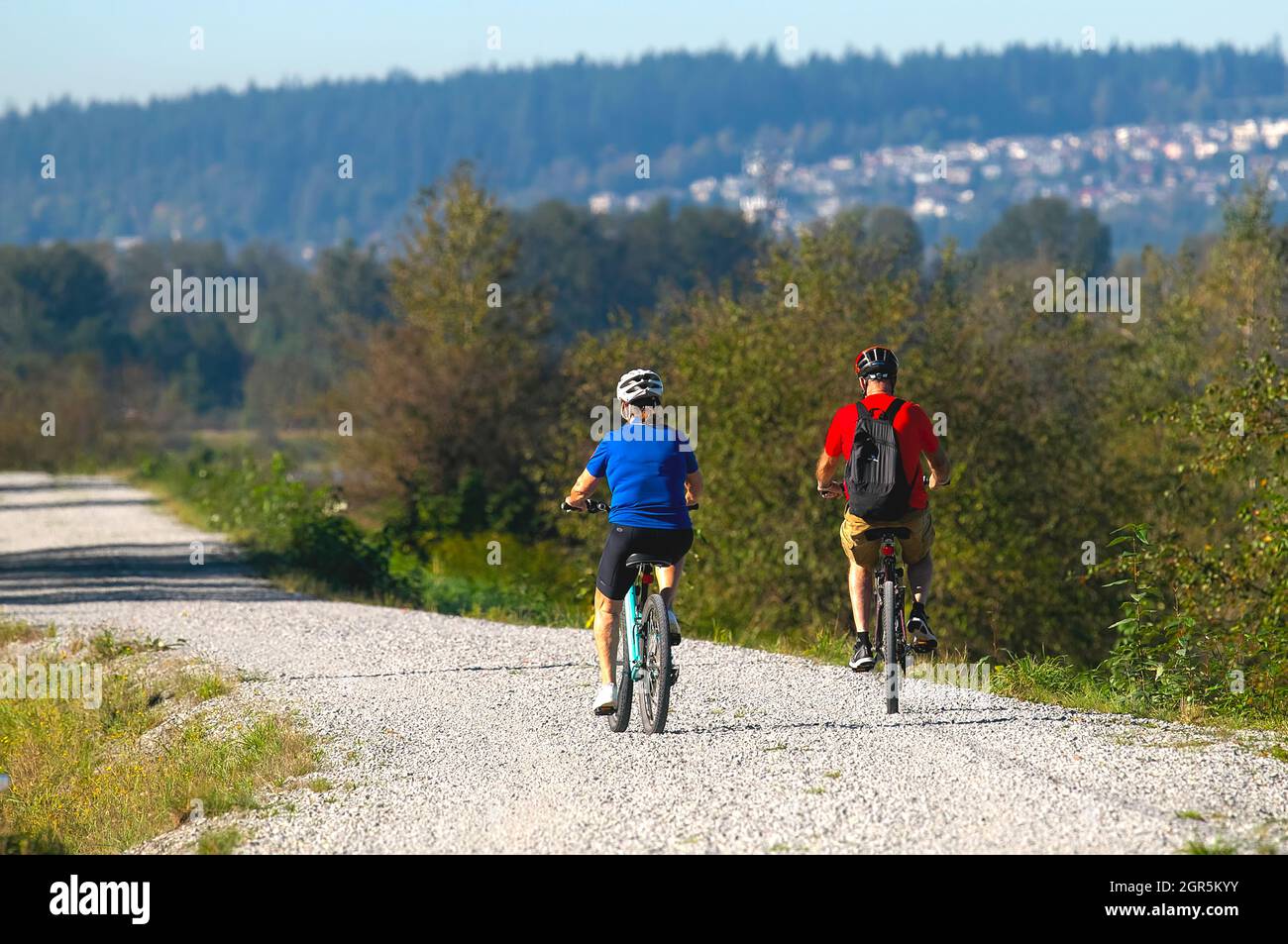 A man and woman riding bicycles on a gravel path facing away. Stock Photo