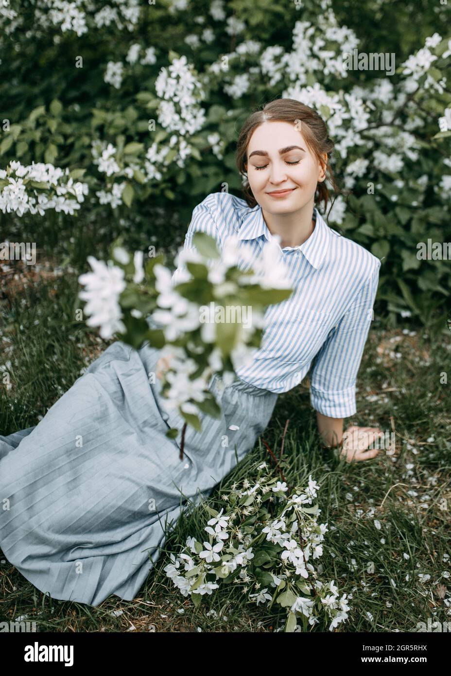 Beautiful Pretty Young Woman Walks Enjoying The Aroma Of Blooming Apple Flowers In A Spring Park Stock Photo
