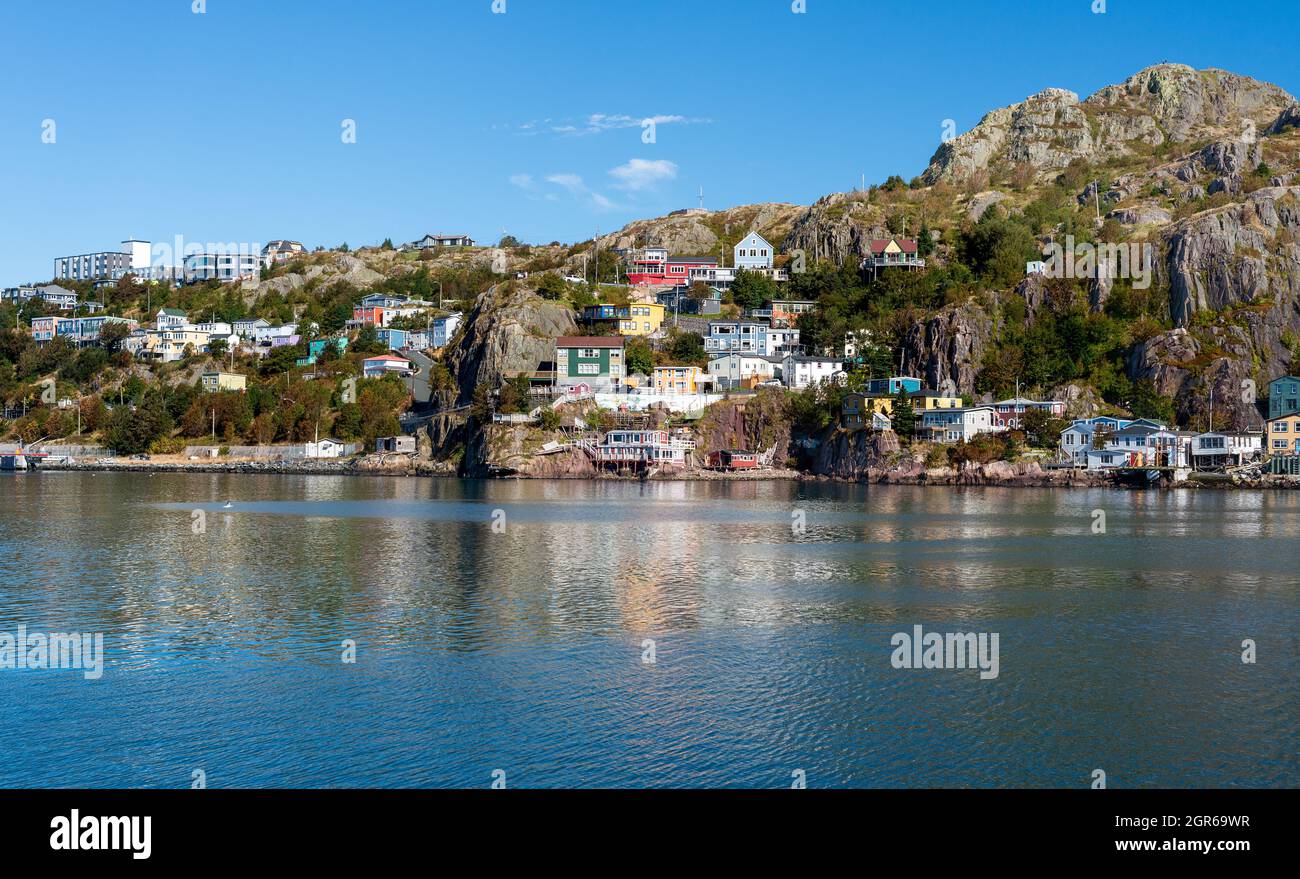 The hillside of St. John's Harbour, on a sunny day, under blue sky and white clouds. The colorful wooden houses are scattered along the hillside. Stock Photo