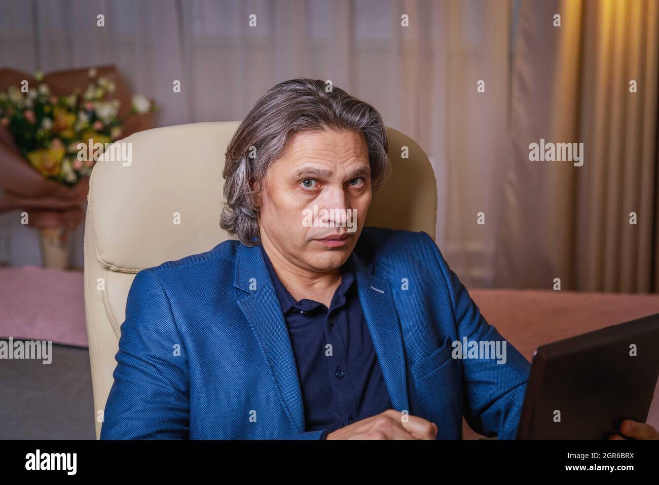 A 50-year-old Man With Long Gray Hair Works At A Computer. Works At Home, Remotely. Stock Photo