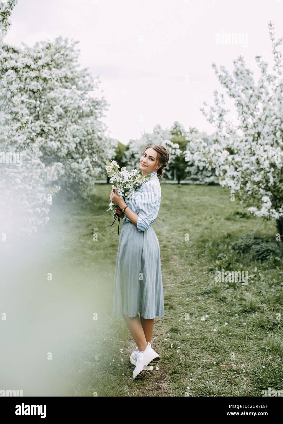 Beautiful Pretty Young Woman Walks Enjoying The Aroma Of Blooming Apple Flowers In A Spring Park Stock Photo