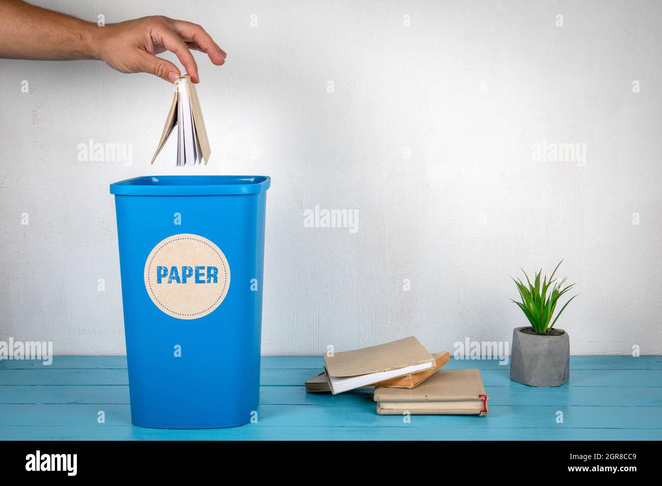 Paper sorting and recycling. Man's hand throws a book in a blue trash