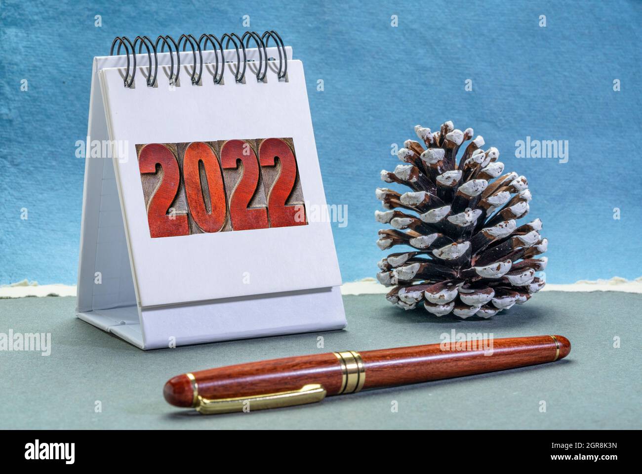 2022 number in letterpress wood type on a spiral desktop calendar with a decorative frosty pine cone against handmade paper, New Year, time management Stock Photo