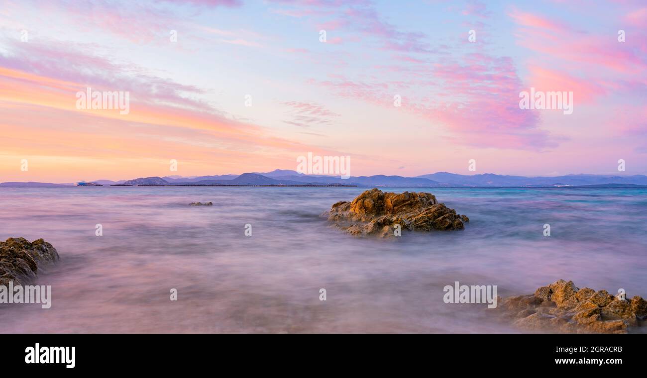 Stunning seascape with a romantic and relaxing sunrise reflected on a calm water flowing in the foreground. Golfo Aranci, Sardinia, Italy. Stock Photo