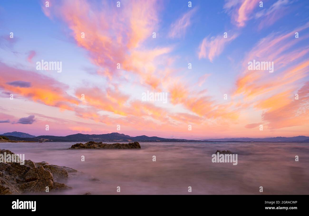 Stunning seascape with a romantic and relaxing sunrise reflected on a calm water flowing in the foreground. Golfo Aranci, Sardinia, Italy. Stock Photo