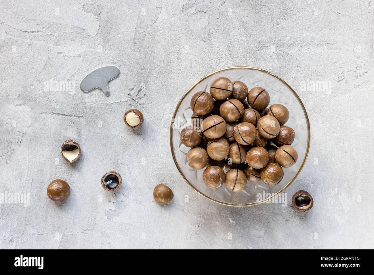 Roasted Salted Macadamia Nuts In Shell In Bowl And Opener On Gray