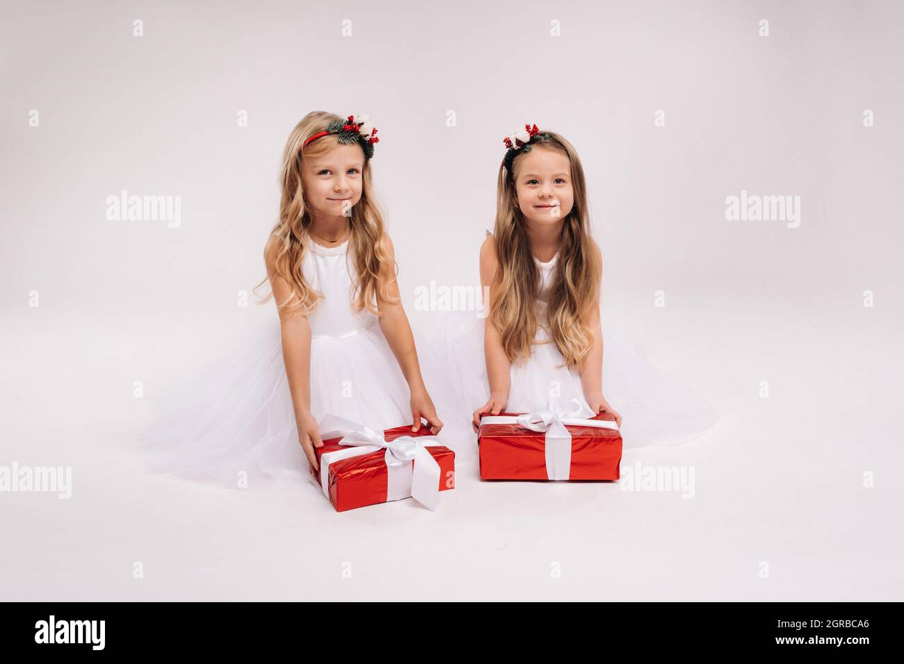 two little girls in white dresses with Christmas gifts on a white ...
