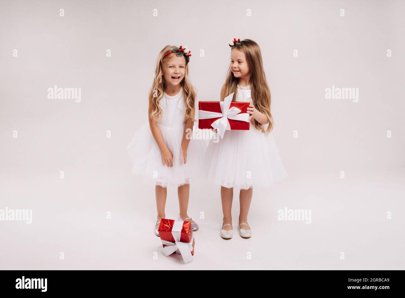 two little girls in white dresses with Christmas gifts on a white ...