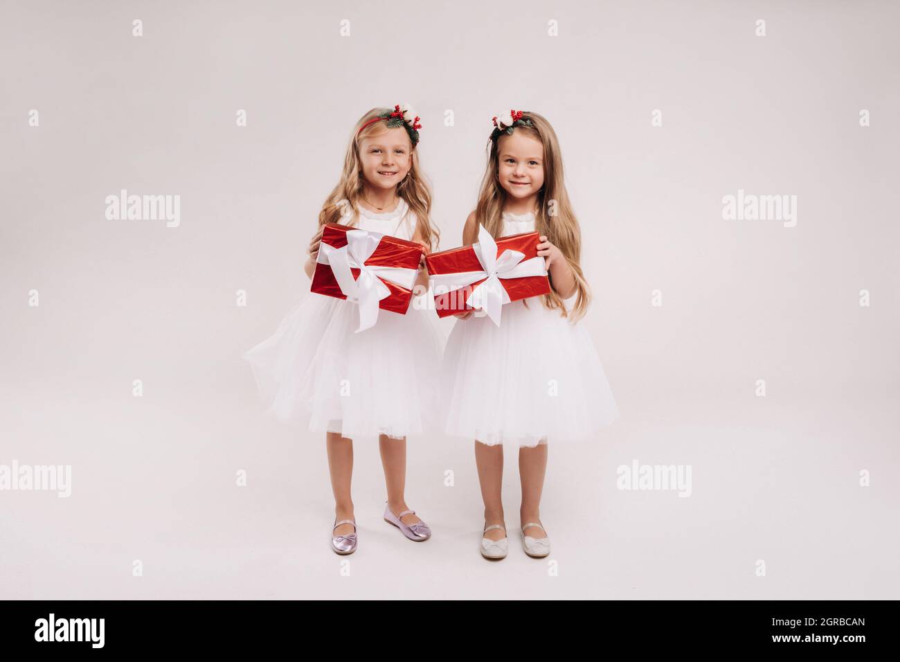 two little girls in white dresses with Christmas gifts on a white ...