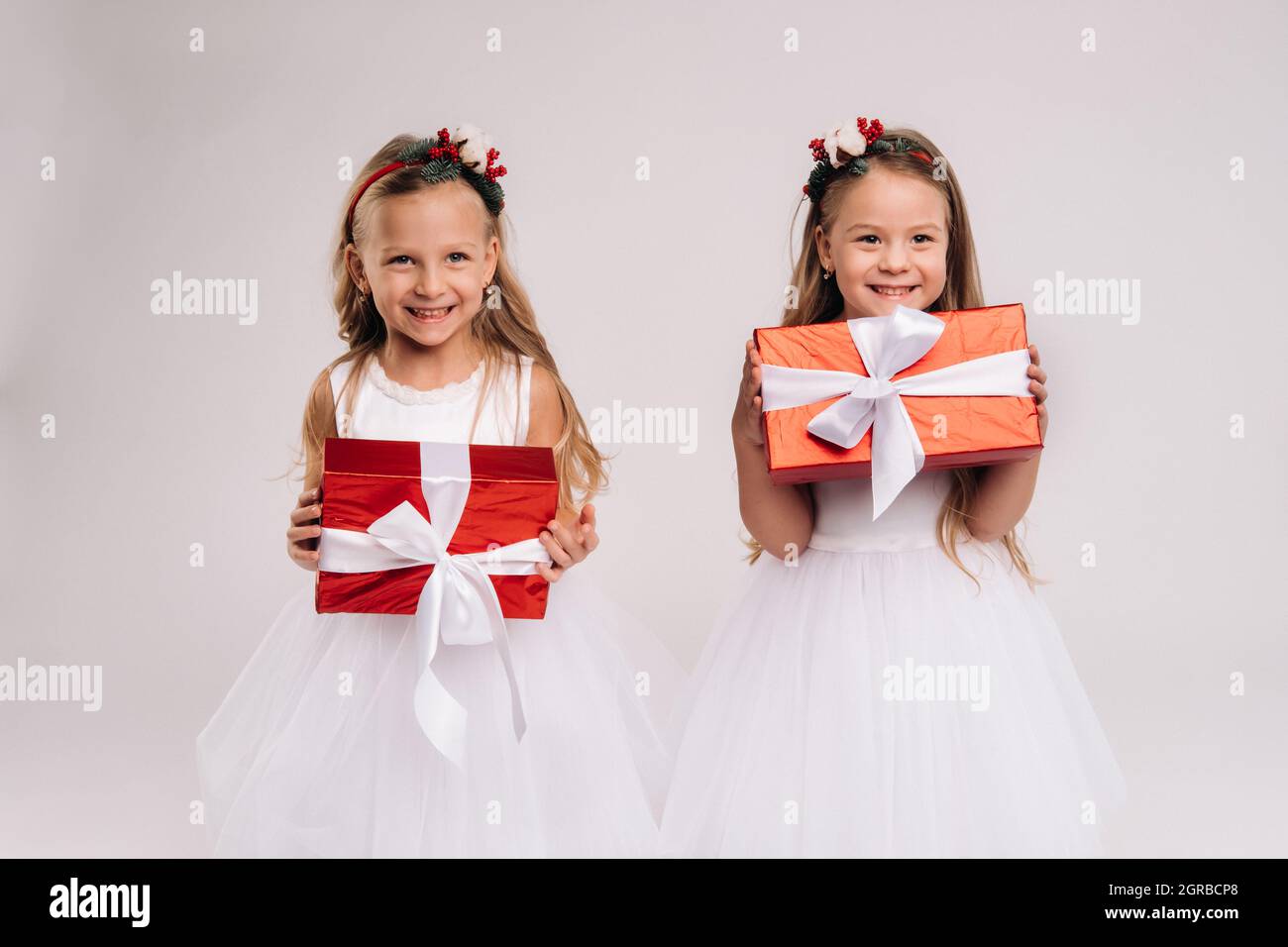 two little girls in white dresses with Christmas gifts on a white ...