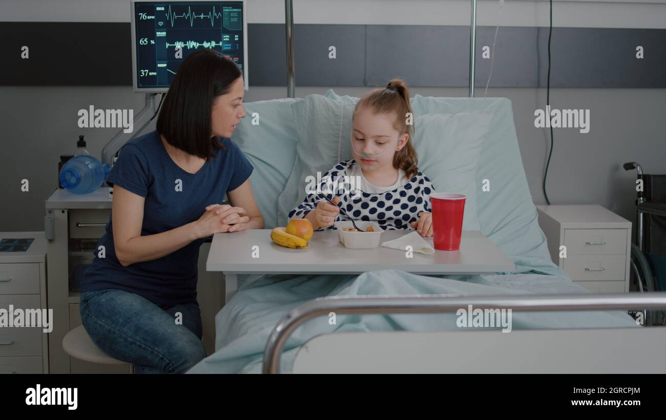 Mother sitting with sick child patient while eating healthy food lunch
