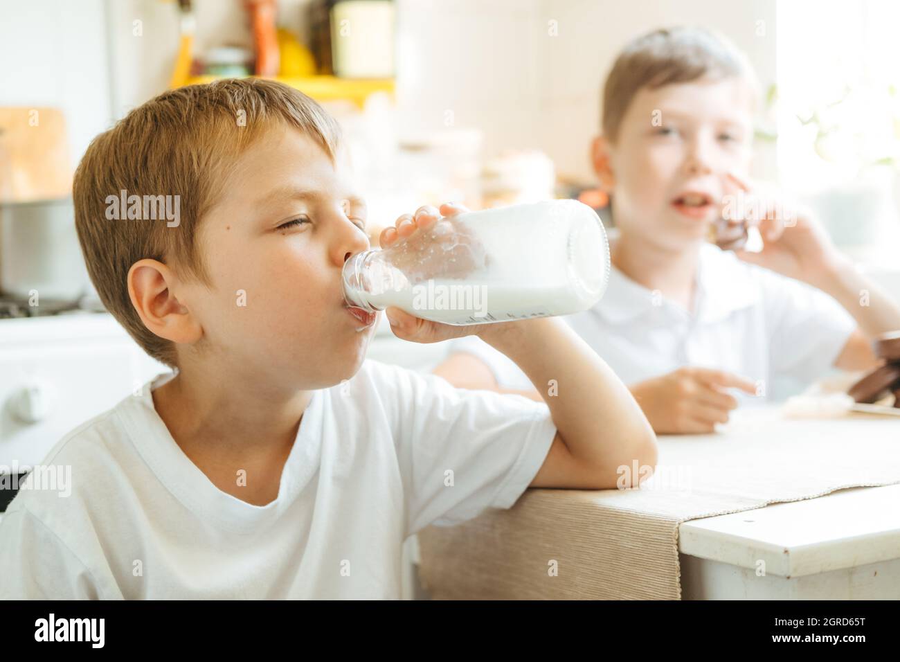A boy is drinking milk from a bottle in the kitchen at home. Morning