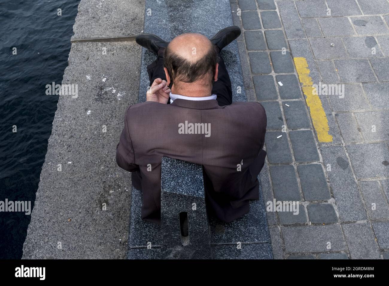 Shot of an adult man with a cavity sitting on a sidewalk near water ...