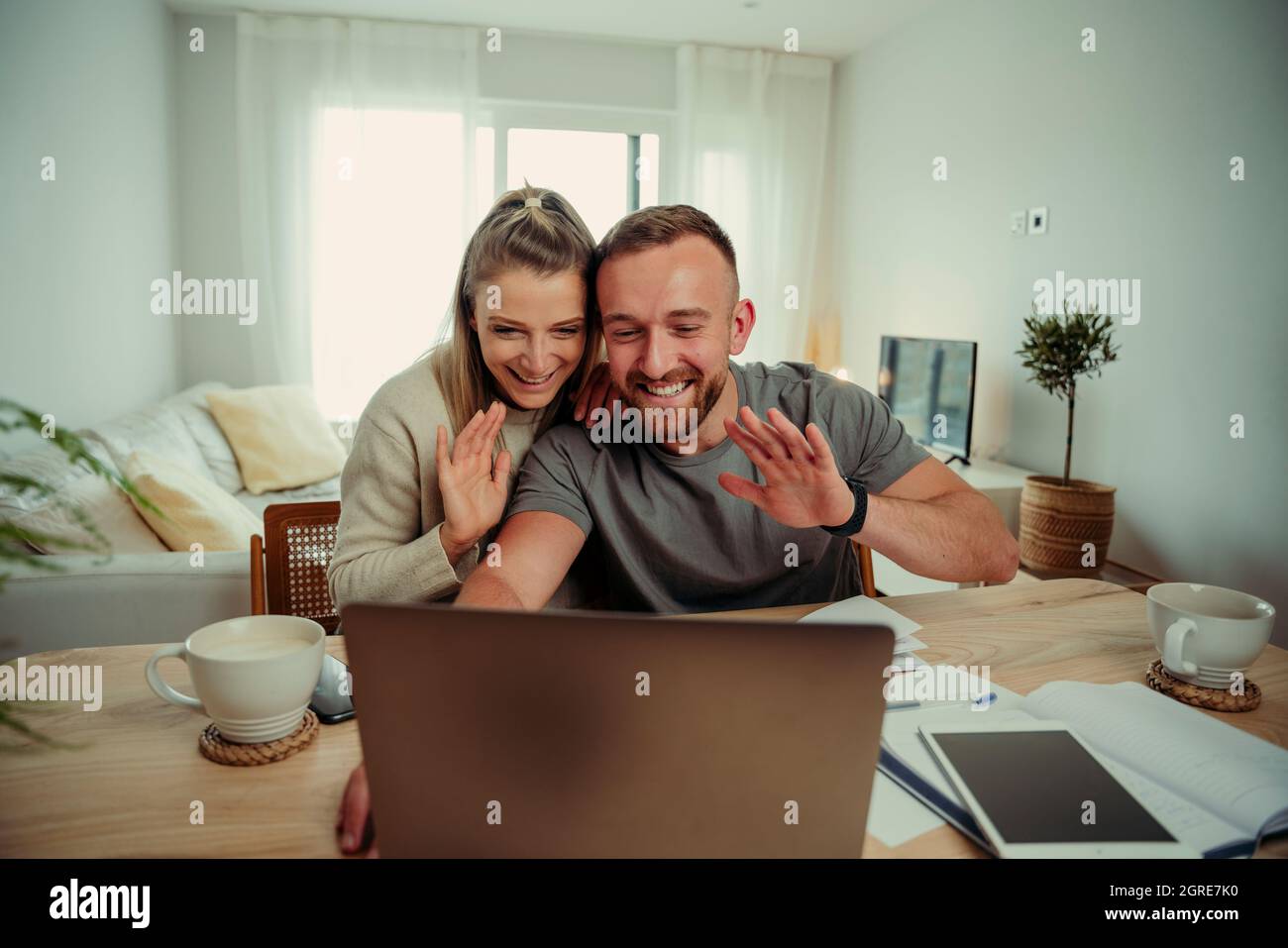 Caucasian happy couple sitting in living room waving to laptop while on video call with family Stock Photo