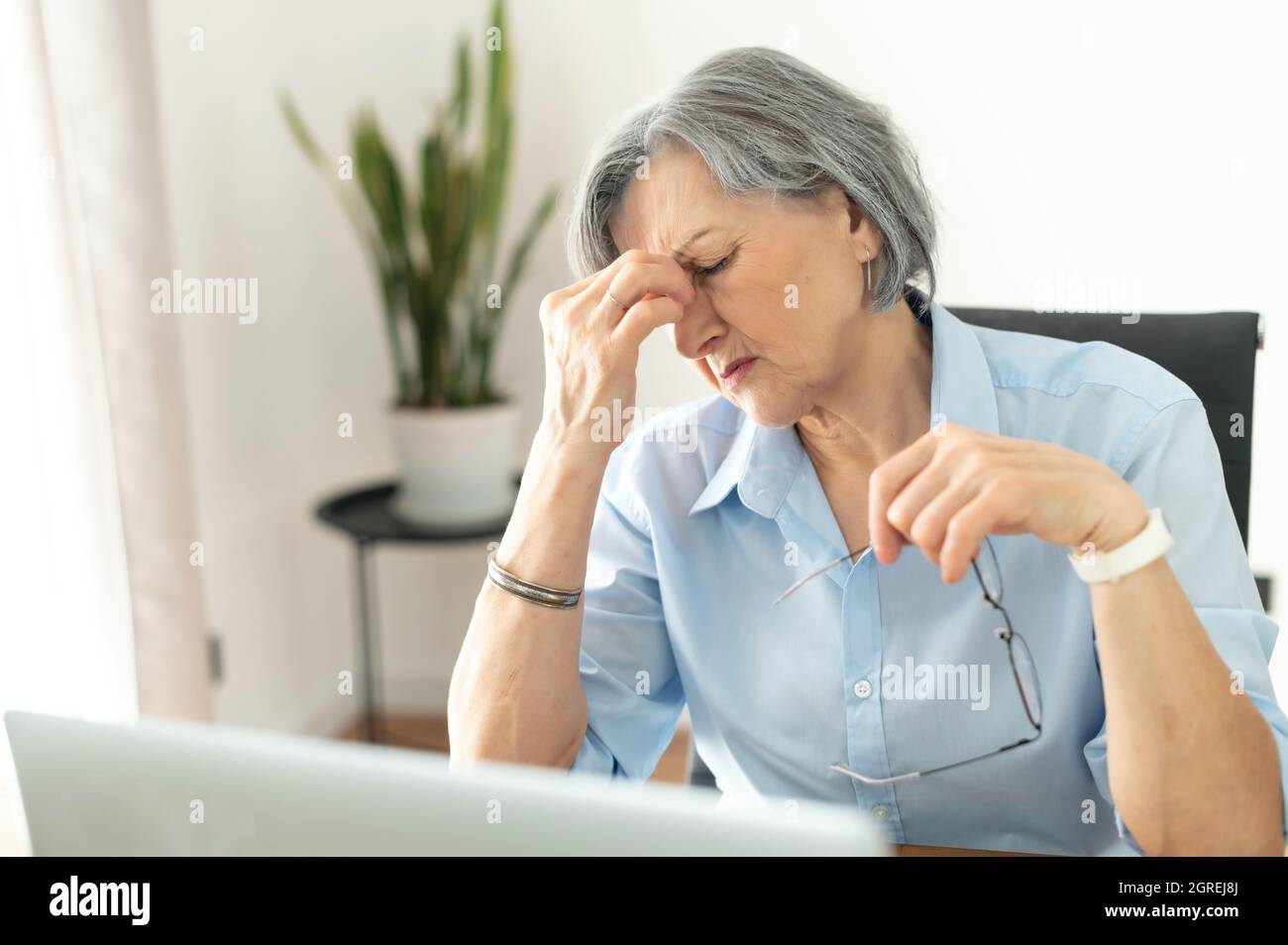 Tired and overworked stressed mature woman working on laptop at home indoor, female teacher feeling exhausted after lecturing students online, touching eyes. Smart working senior people and technology Stock Photo