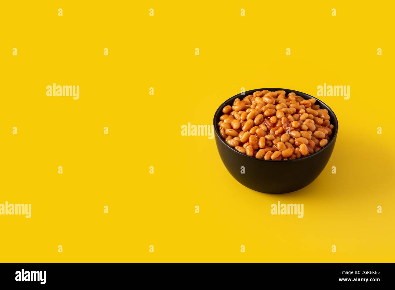 White beans in tomato sauce in bowl isolated on yellow background Stock