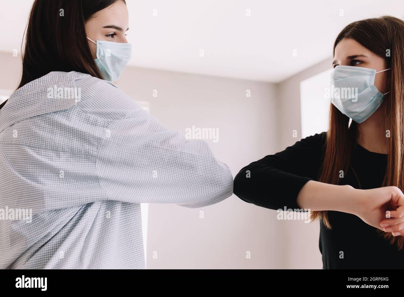 Two Smiling Girls In Protective Face Mask Say Hello In Safe Way With Their Elbow. High Quality Photo Stock Photo