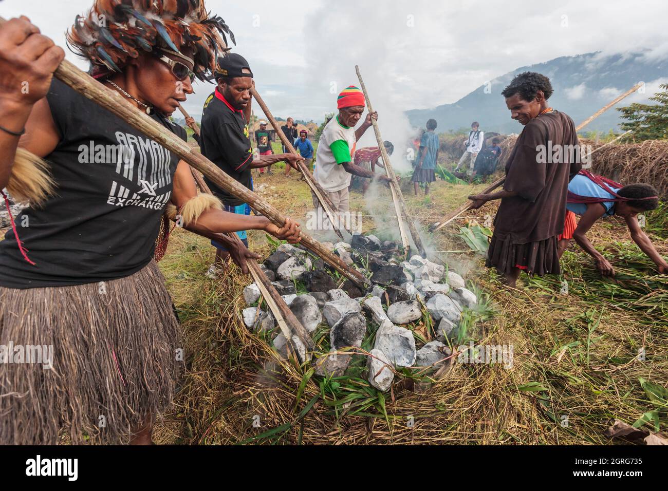 Indonesia, Papua, city of Wamena, members of the Dani tribe perform traditional cooking of sweet potatoes in an earth oven, with stones heated by wood fire and wrapped in plant leaves. Baliem Valley Cultural Festival, every August, tribes come together to perform ancestral war scenes, parade and dance in traditional clothes Stock Photo
