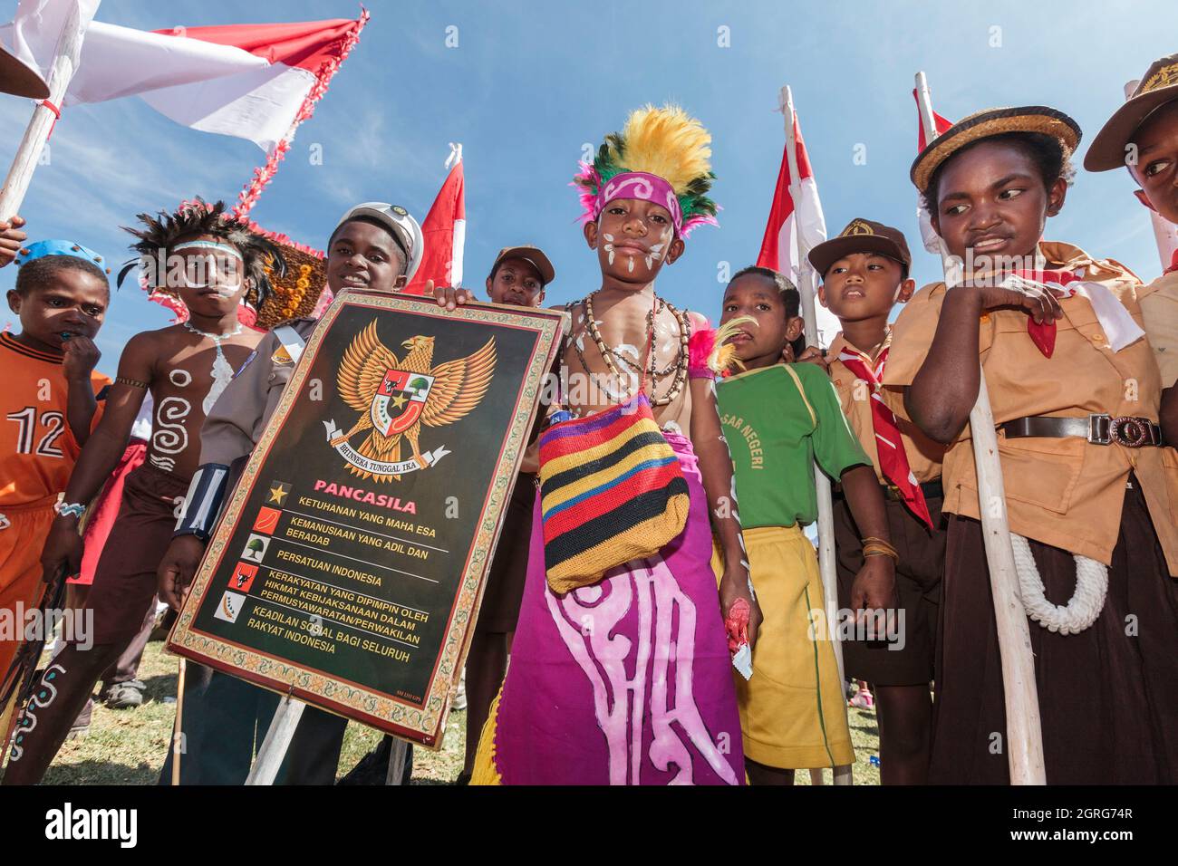 Indonesia, Papua, downtown Wamena, children's parade, celebration of Indonesia's Independence Day. Each tribe is invited to showcase its culture through dances and traditional clothing, in order to strengthen the feeling of cultural freedom. The sign features the national embleme of Indonesia and its motto: Unity in diversity. Stock Photo