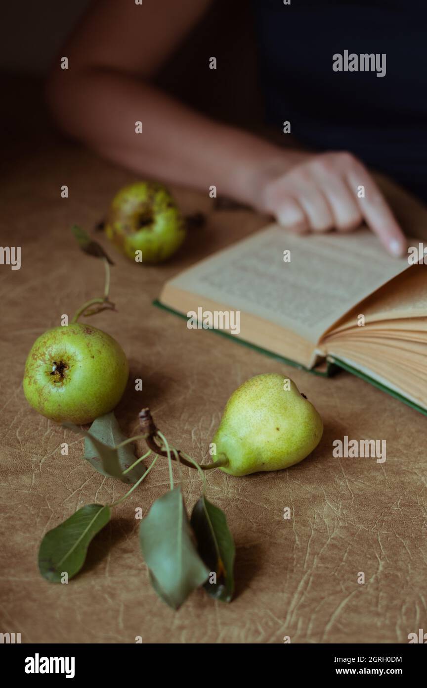 Green pears and a woman reading a book at a table, brown tones Stock Photo