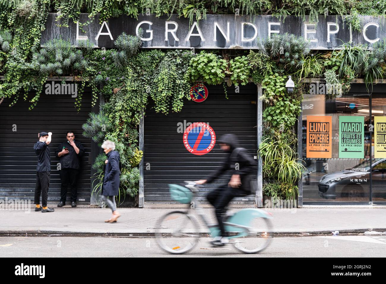 A man rides a Velib bicycle in front of the green wall of La Grande  Epicerie de Paris, located in the 16th district of Paris. Paris France,  October 1st, 2021. Photo by