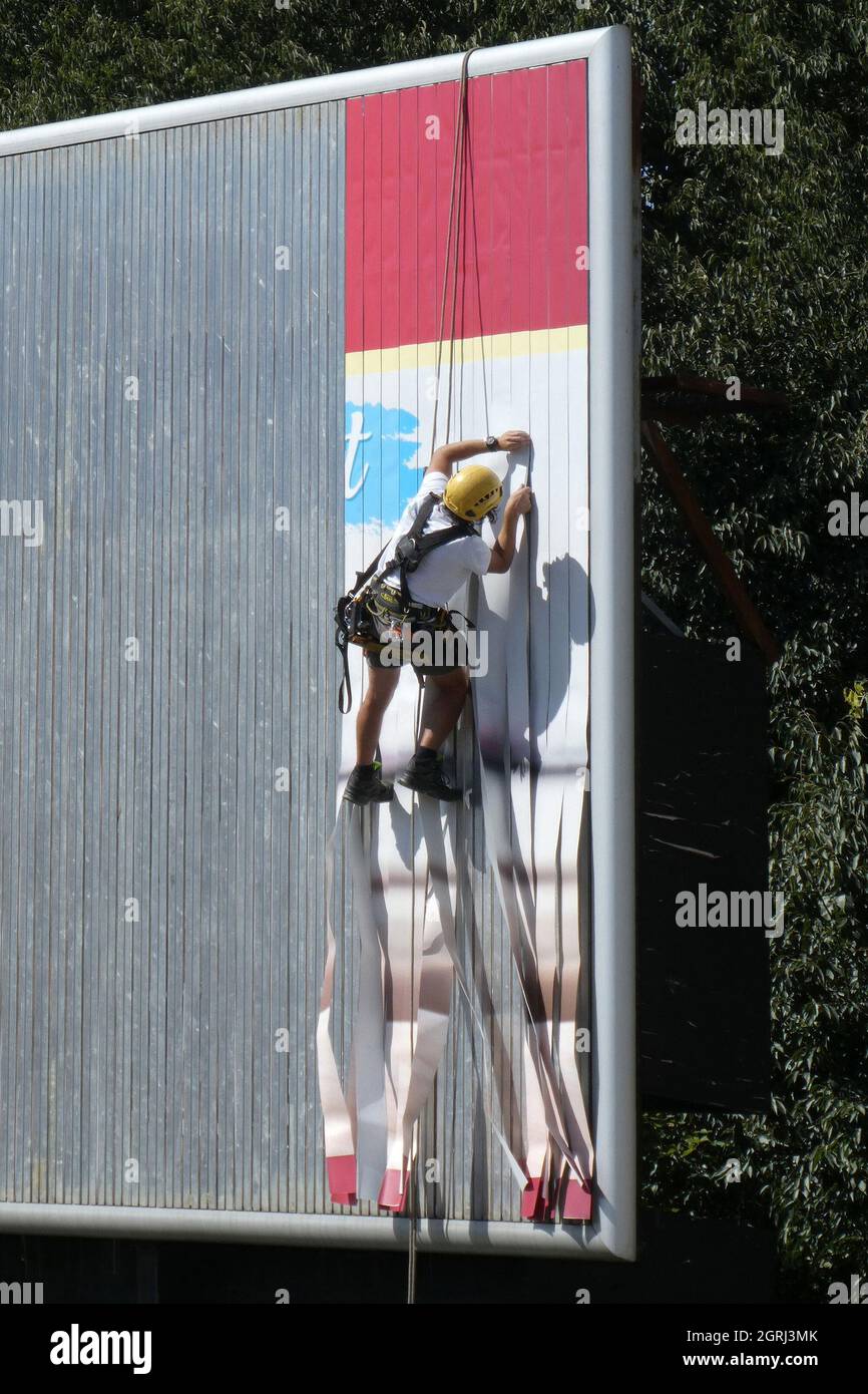 NOVI SAD, SERBIA - Sep 08, 2021: A vertical shot of a worker changing an advertisement on a billboard in Novi Sad, Serbia Stock Photo
