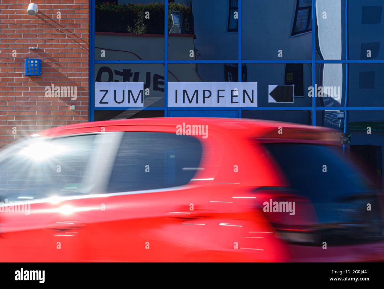 Aue, Germany. 01st Oct, 2021. A sign 'Zum Impfem' sticks to the window of a shopping center while a car drives towards the 'Drive Impf'. In cooperation with the German Red Cross (DRK), the Simmel Center and the Great District City of Aue-Bad Schlema, a mobile vaccination team is available today in the parking lot for vaccination against the coronavirus. Credit: Robert Michael/dpa-Zentralbild/dpa/Alamy Live News Stock Photo