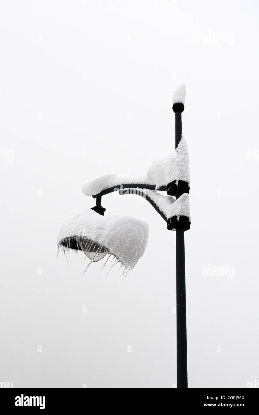 Lamp post covered in fresh snow with icicles bent by the wind hanging off it against a monochrome high key lighting sky Stock Photo