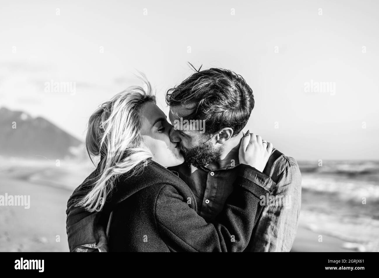 Romantic hipster couple in love kissing on shoreline at the wild beach - Boyfriend and girlfriend wearing cool clothing and vintage backpack kissing i Stock Photo