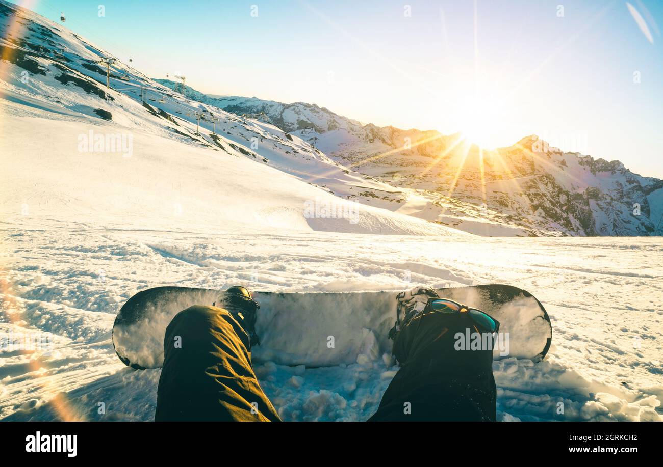 Snowboarder sitting at sunset on relax moment in french alps ski resort - Winter sport concept with adventure guy on top of mountain ready to ride Stock Photo