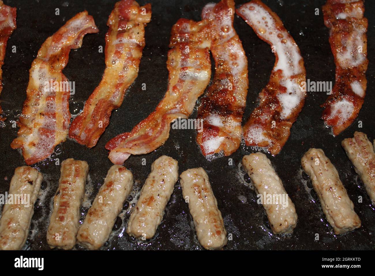Bacon and sausage cooking on a griddle. Stock Photo