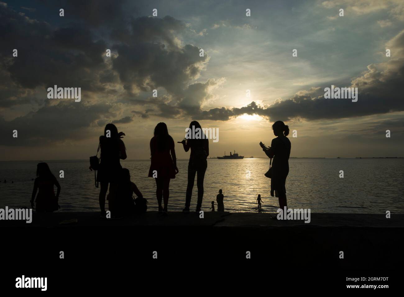 Youngster girls taking photos with their smartphones of the sunset at Manila Bay, Manila, Philippines. Stock Photo