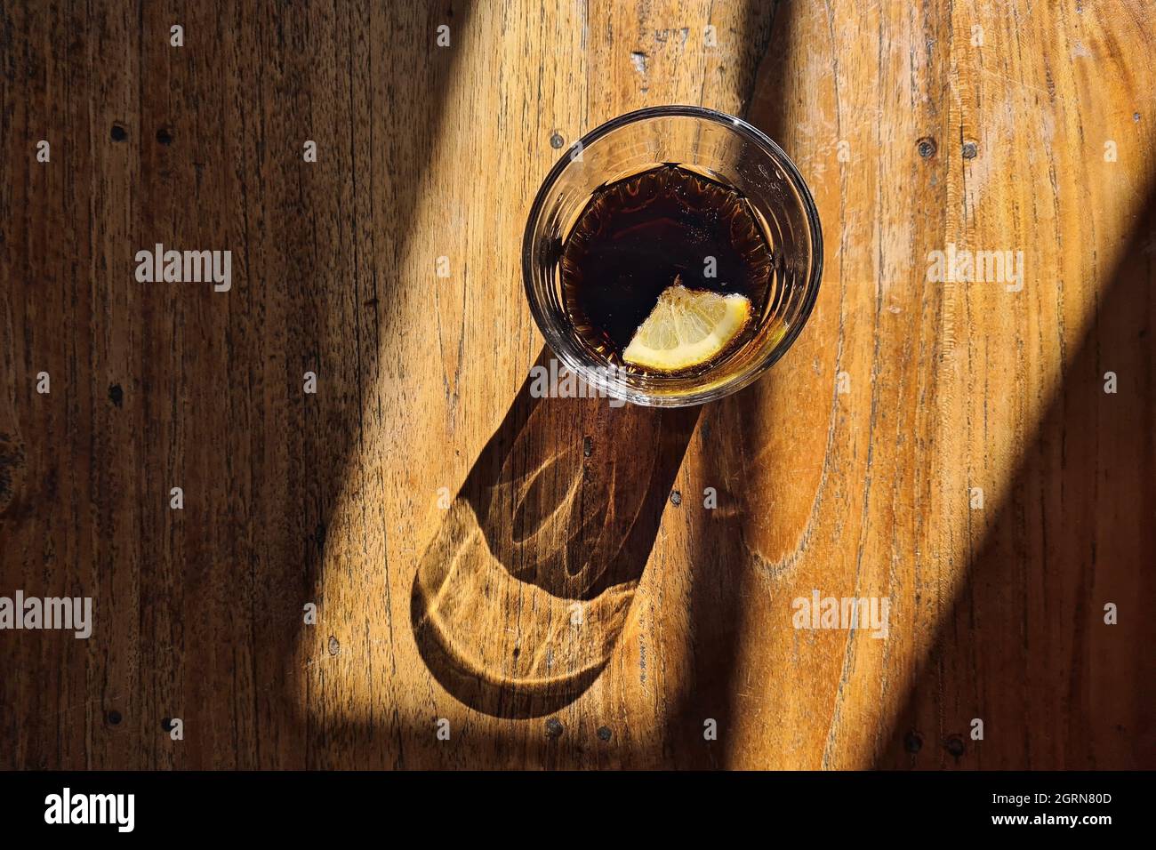 Drinking glass with cola drink. Light and shadow on wooden table. Stock Photo