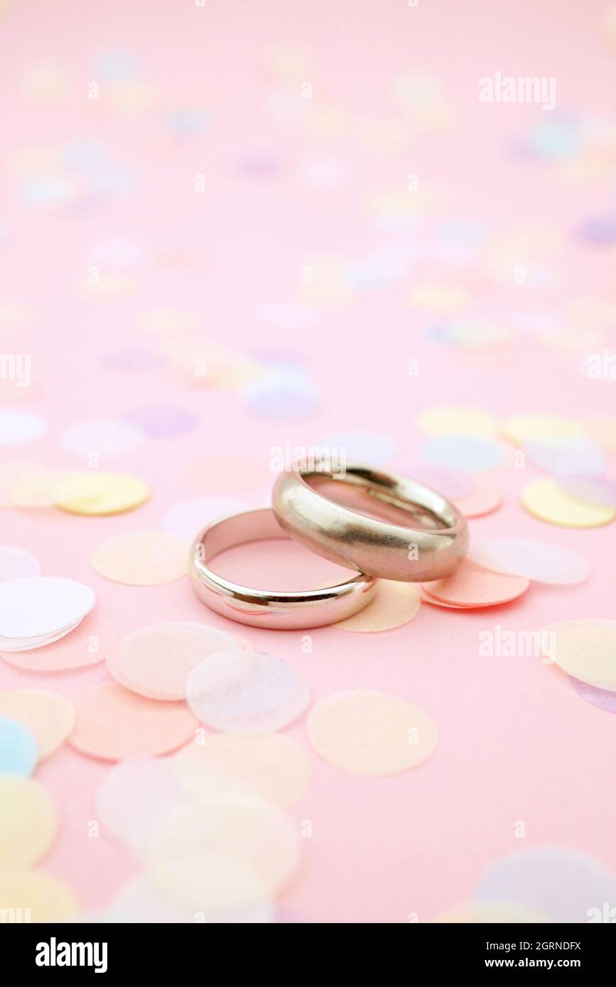 High Angle View Of Wedding Rings And Confetti On Pink Background Stock Photo