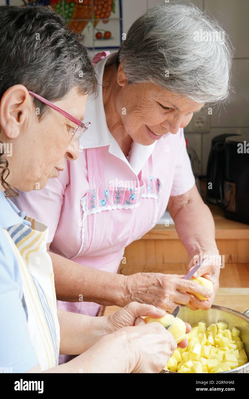 Senior Women Cutting Potatoes In Kitchen Home Stock Photo