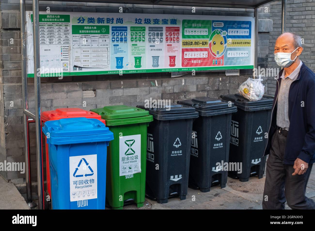Chinese man walks past the bins for sorting garbage in a Hutong in Beijing, China. 01-oct-2021 Stock Photo
