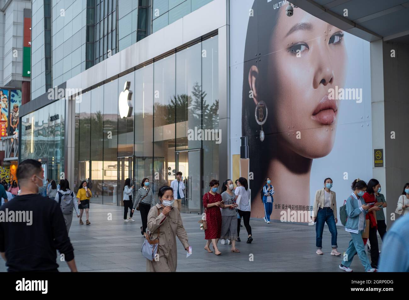Chinese consumers walk past UK fashion label Burberry Ad near an Apple store in Beijing, China.01-Oct-2021 Stock Photo