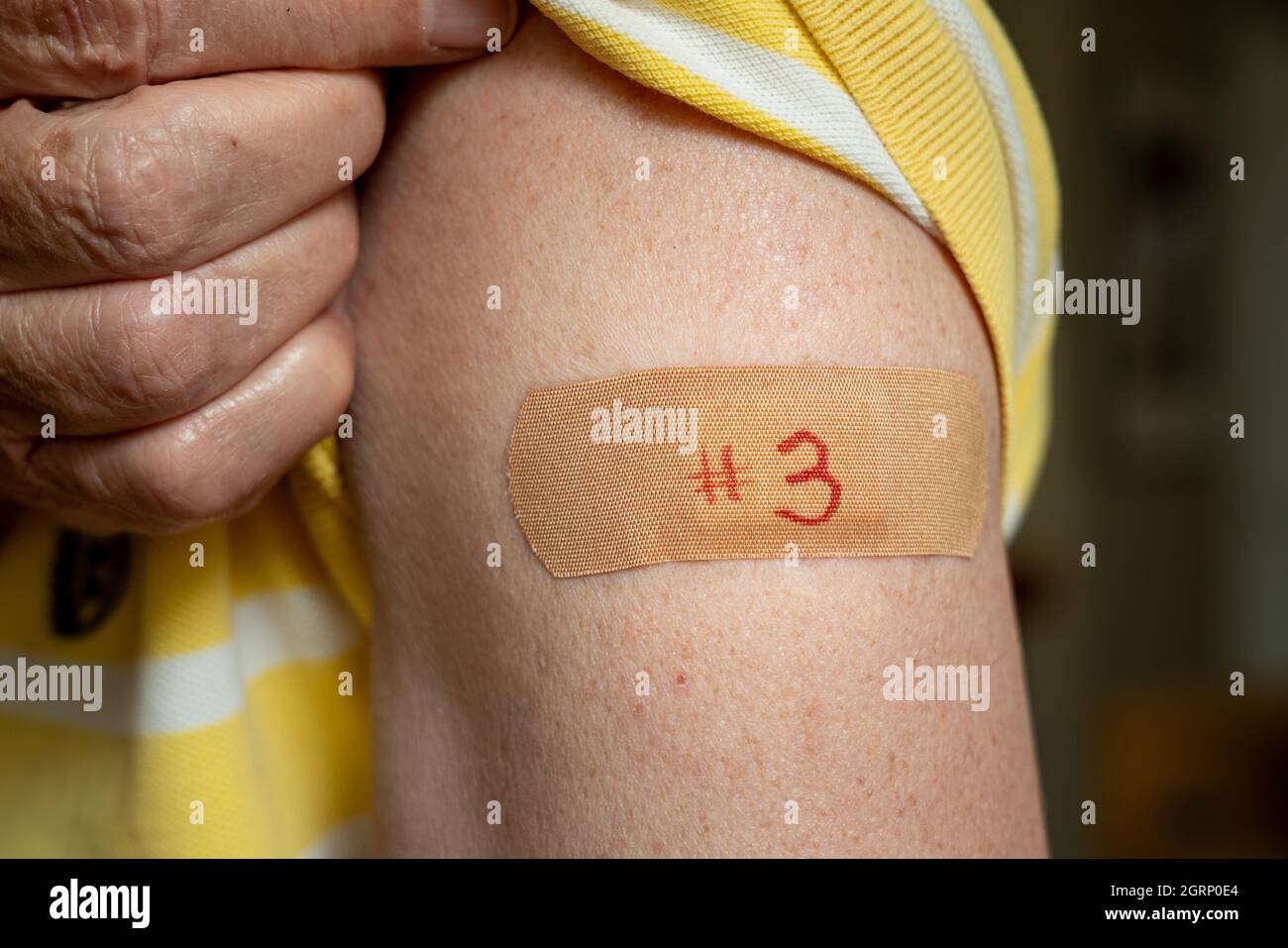 Senior caucasian man holding up shirt sleeve to show the bandaid after the booster coronavirus vaccine shot in the shoulder Stock Photo
