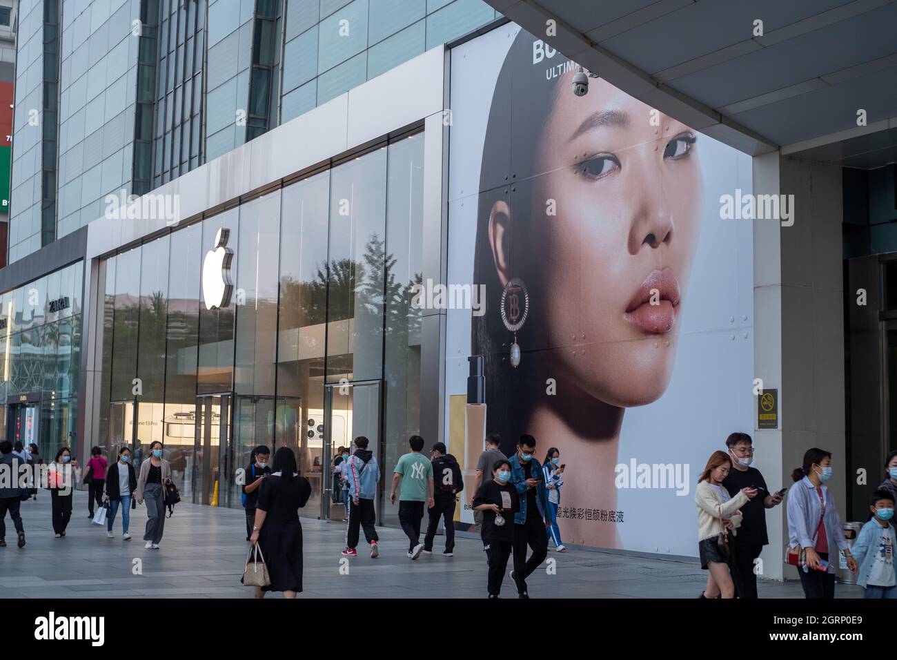 Chinese consumers walk past UK fashion label Burberry Ad near an Apple store in Beijing, China.01-Oct-2021 Stock Photo