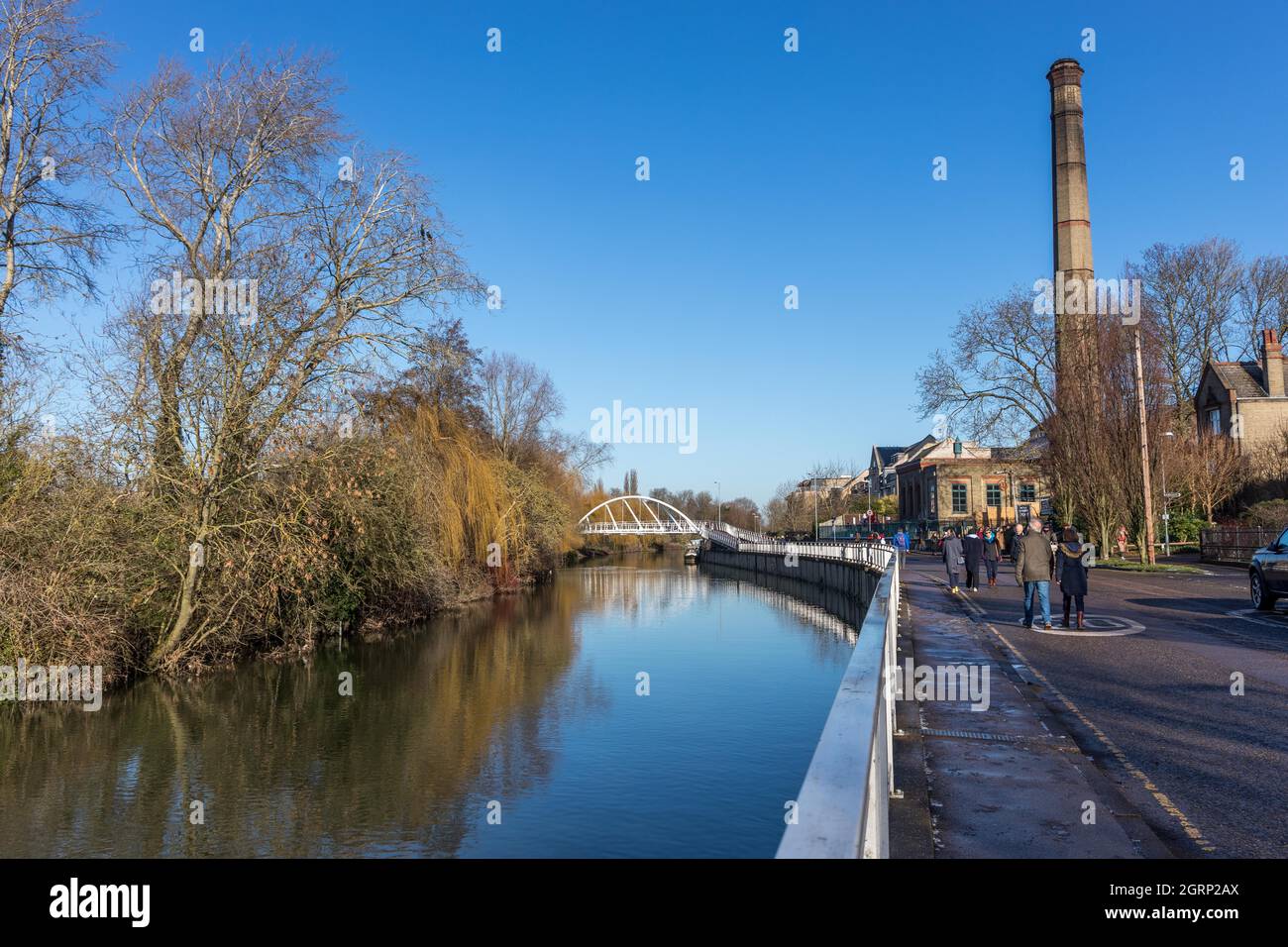 View of calm river cam with white feet bridge and the large old chimney part of the Pumping Station at the Cambridge Museum of Technology on Riverside Stock Photo