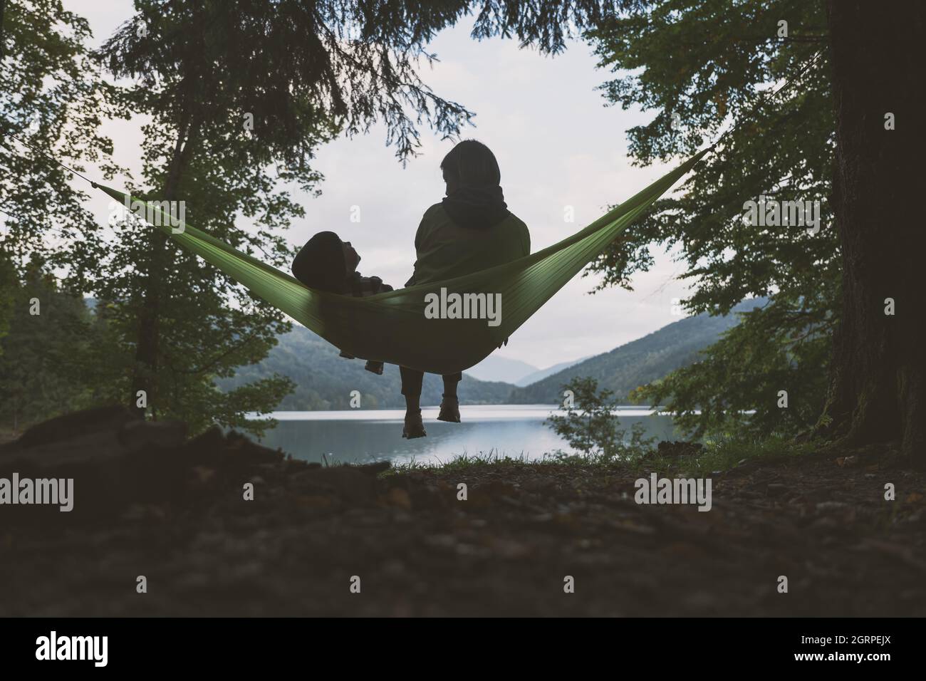 Small kid with mother on hammock on forest lake background. Childhood with nature loving concept Stock Photo