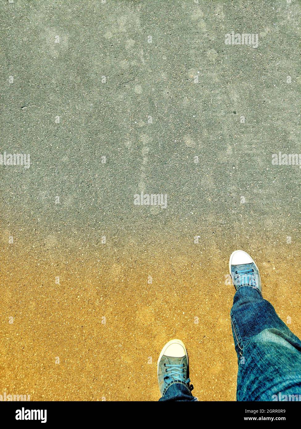 Low Section Of Man Wearing Shoes While Standing At Beach Stock Photo