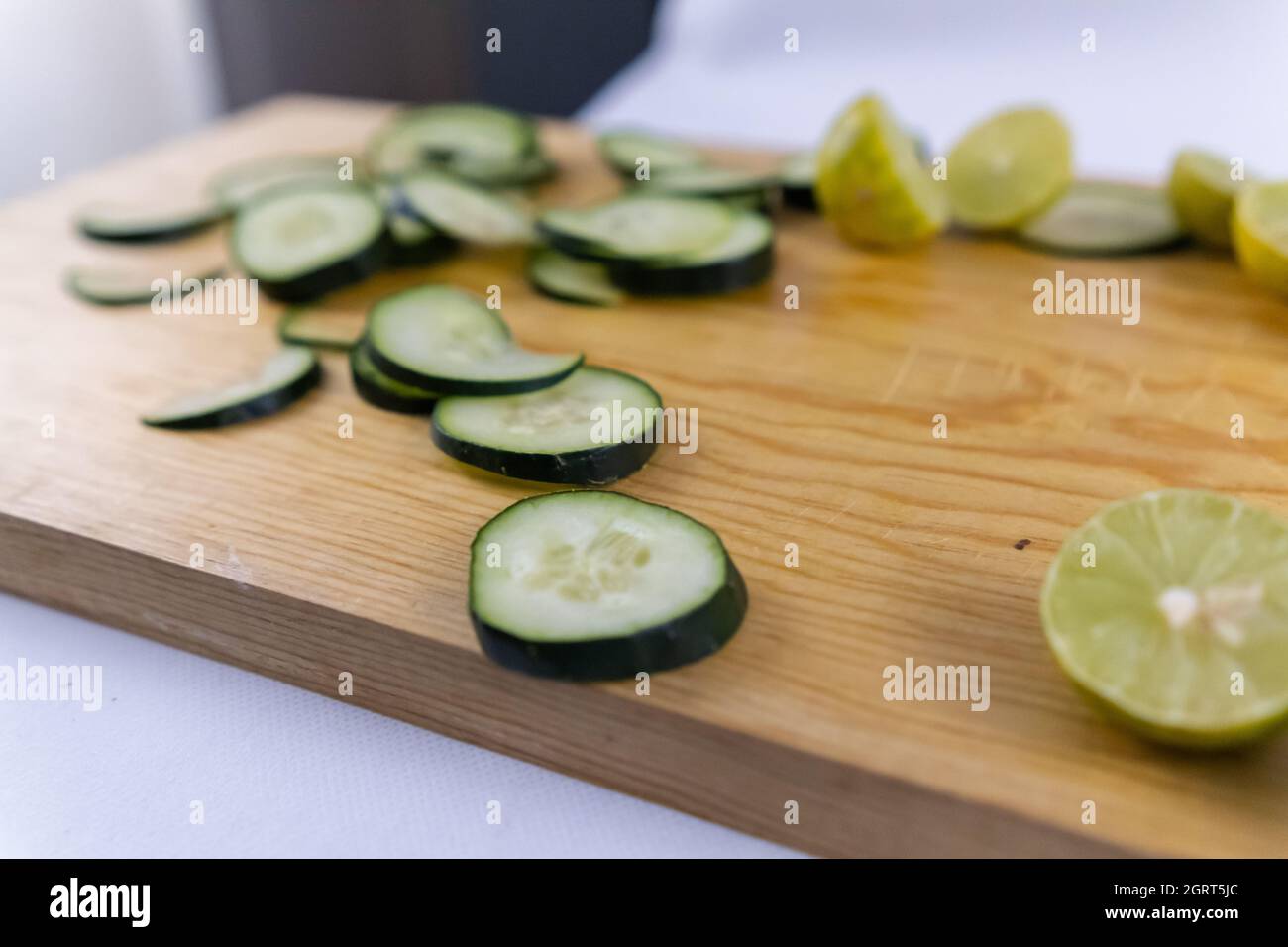 Fresh cucumber slices and a lime cut in half on wooden cutting board Stock Photo