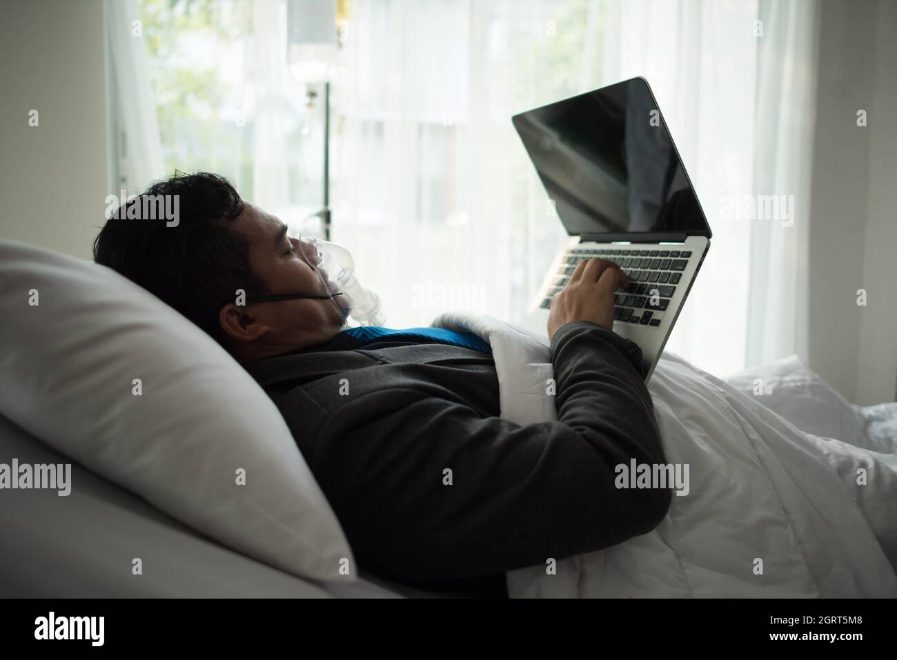 Businessman Using Laptop Lying Down On Bed At Hospital Stock Photo Alamy